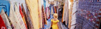 Colorful traveling by Morocco. Young woman in yellow dress walking in medina of blue city Chefchaouen.