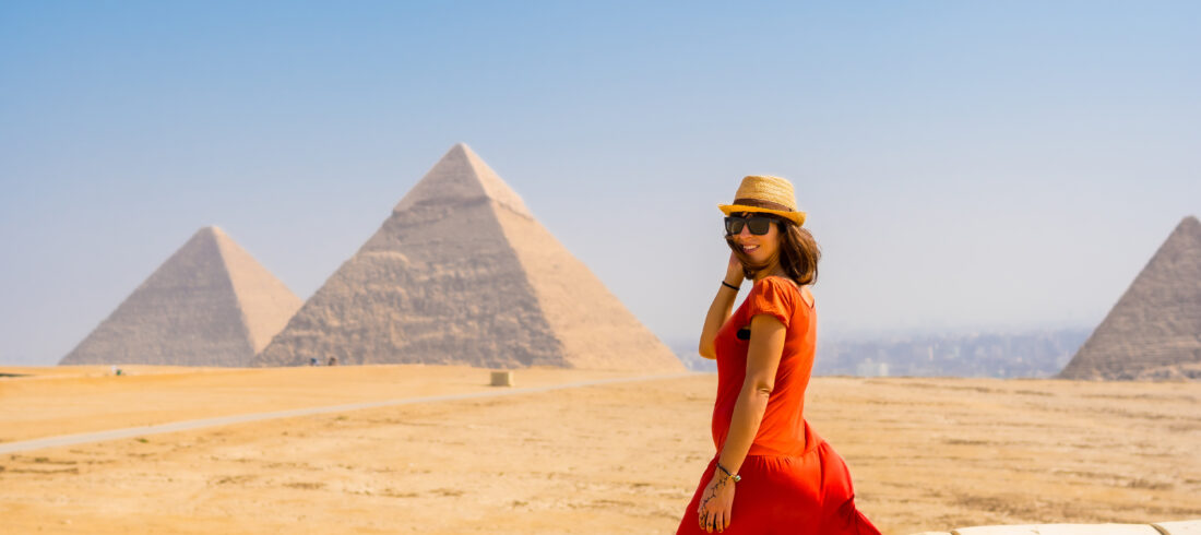 A tourist girl in a red dress at the Pyramids of Giza, the oldest Funerary monument in the world. In the city of Cairo, Egypt