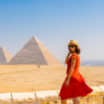A tourist girl in a red dress at the Pyramids of Giza, the oldest Funerary monument in the world. In the city of Cairo, Egypt
