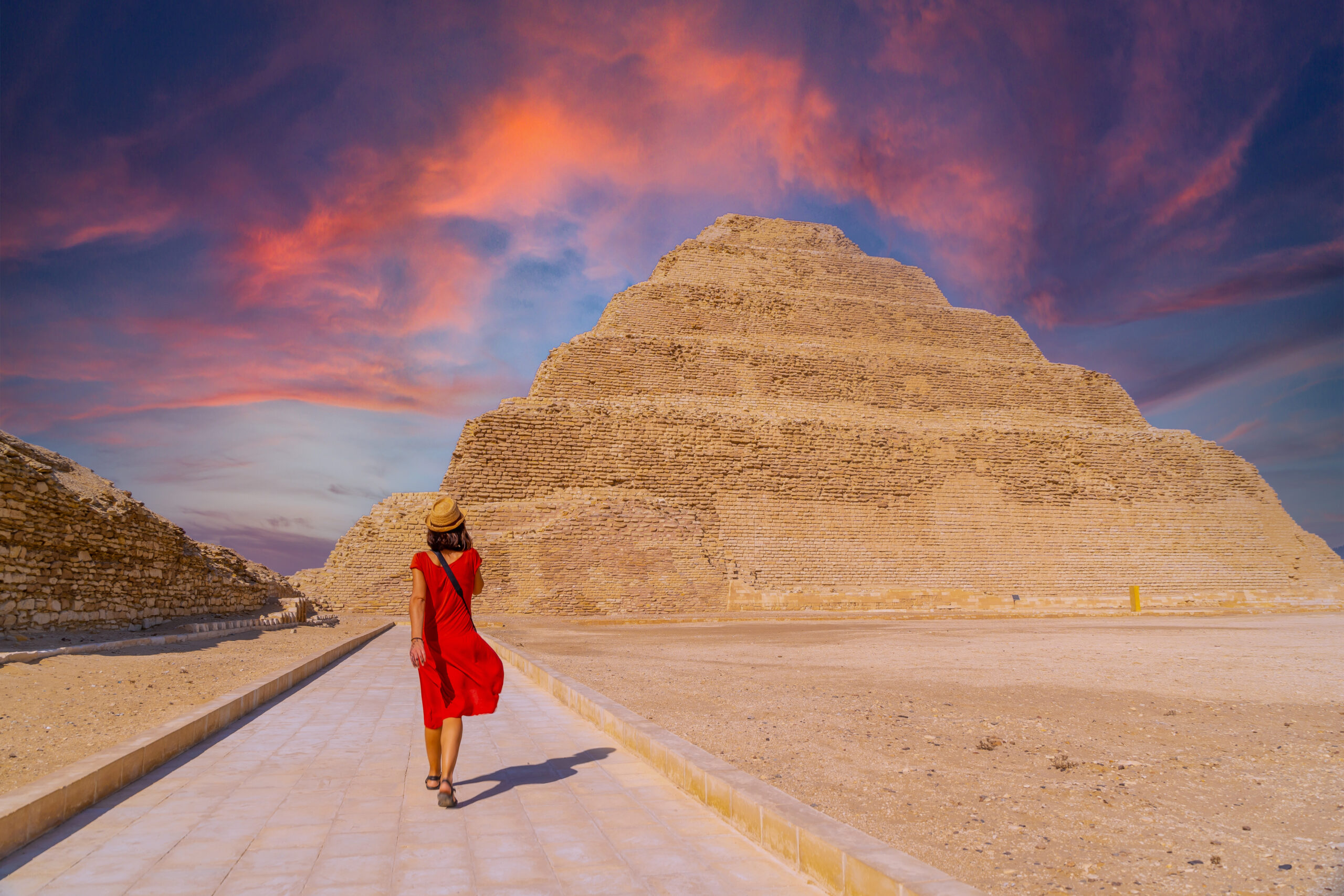 A young tourist in a red dress at the Stepped Pyramid of Djoser at sunset, Saqqara. Egypt. The most important necropolis in Memphis. The first pyramid in the world